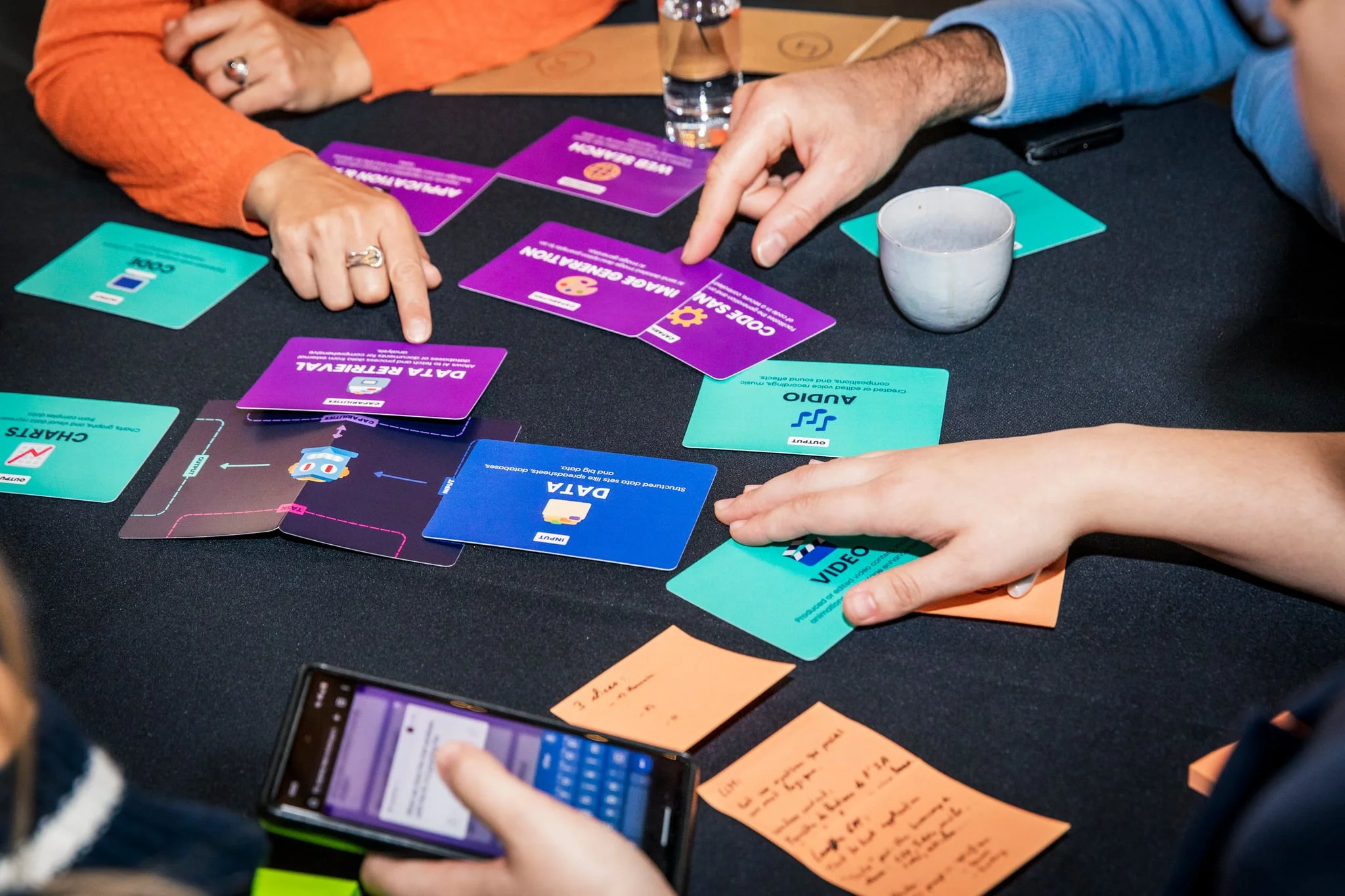 Workshop participants arranging colorful AI Tinkerers cards into combinations on a table.